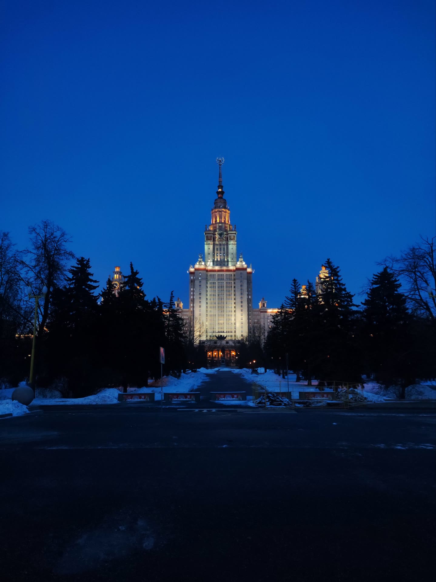 the msu main building lit up at blue hour, firs in silhouette and snow banked along an empty road