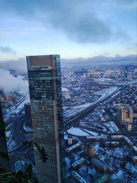 a neighbouring moscow-city tower from above, clouds drifting below it over the snowy city