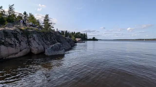 granite cliffs at mon repos, people standing on the rock, the bay opening out with a sailboat far off