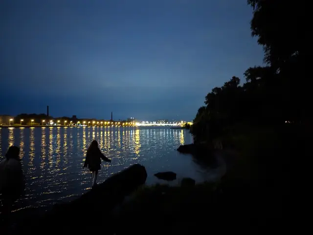 blue hour by the water, a girl walking along a fallen log while city lights streak across the bay