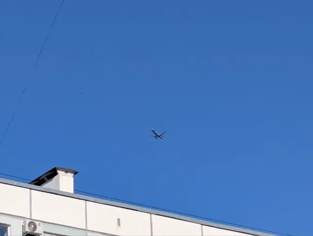 a plane climbing over the roof of a residential block against a clear blue sky