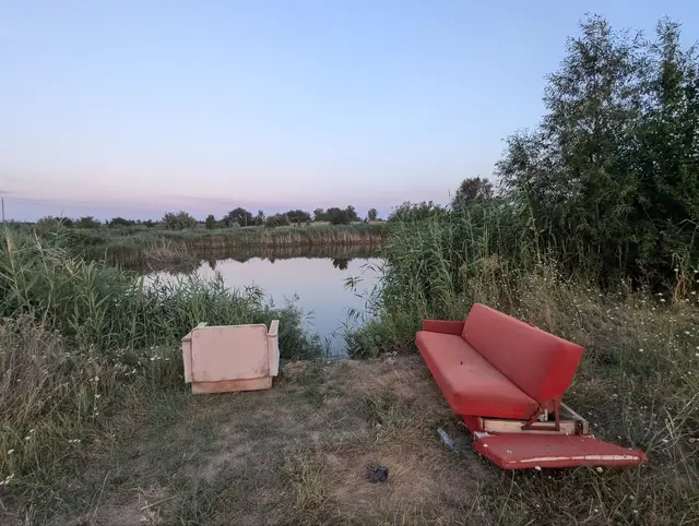 an abandoned red sofa and an armchair left on the bank of a pond at dusk