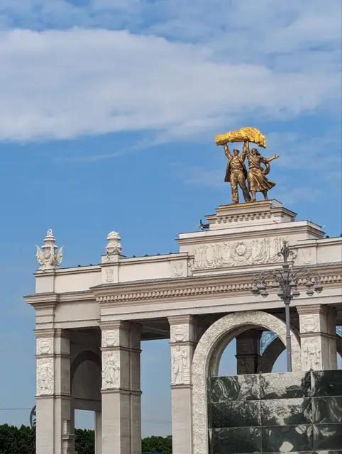 the vdnh main arch with its golden sculpture holding a sheaf against a summer sky
