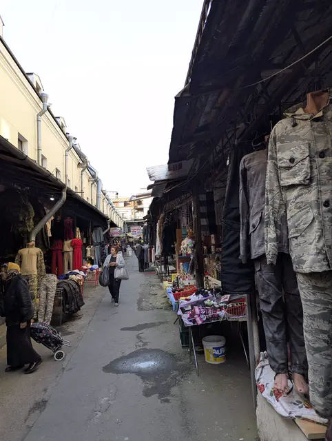 a covered market passage, camouflage trousers and jackets hanging from the awning over the stalls