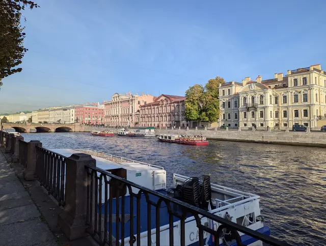 a moored tour boat behind the iron railing of the fontanka, pastel palaces lined up along the far bank
