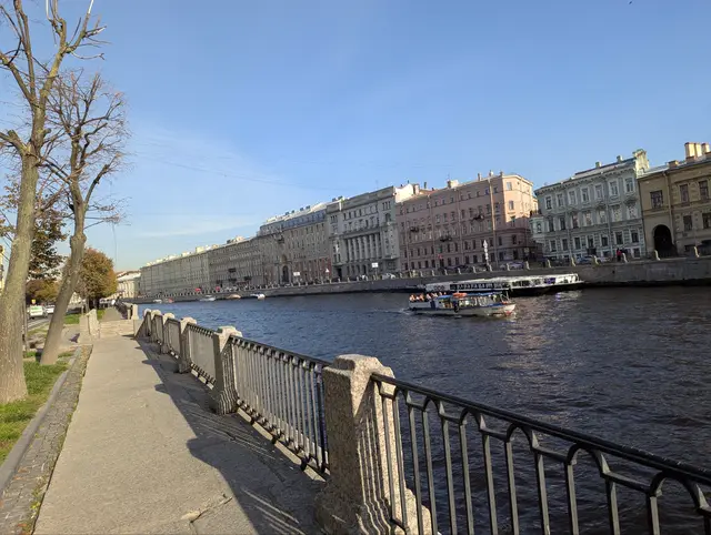 an empty granite embankment with bare trees, a pleasure boat crossing toward a row of facades