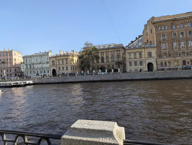 a long run of nineteenth-century facades along the river, a granite post of the railing in the foreground