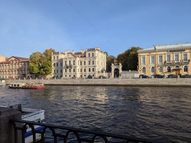 a pale yellow mansion and a stone gateway across the river, a red tour boat passing below