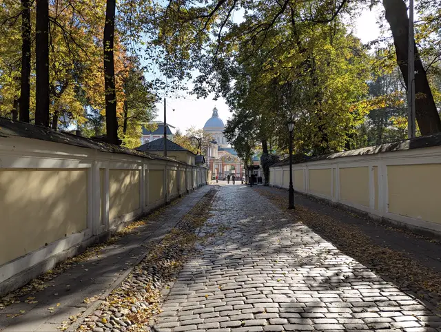 a cobbled lane between two low yellow walls under autumn trees, a cathedral dome at the far end