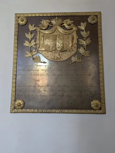 a bronze memorial plaque with a gilded coat of arms and laurel branches on a white wall