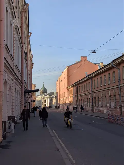 a narrow street of red and pink houses in low sun, a green church dome closing it off at the end