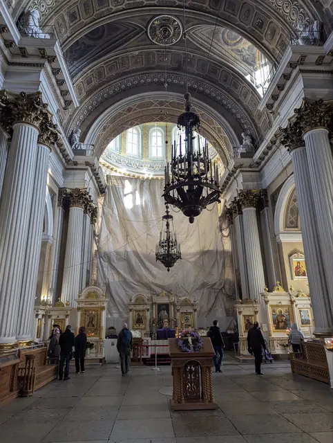 the nave of a classical cathedral, a black iron chandelier hanging under a coffered vault, the altar screen covered for restoration