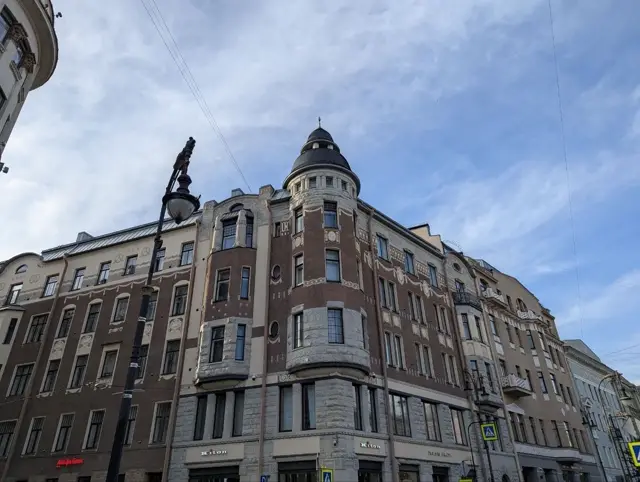 an art nouveau corner building with a dark conical turret, an ornate lamp post in front of it