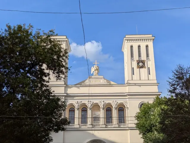 the same church seen through branches, an angel holding a cross on the pediment between the towers