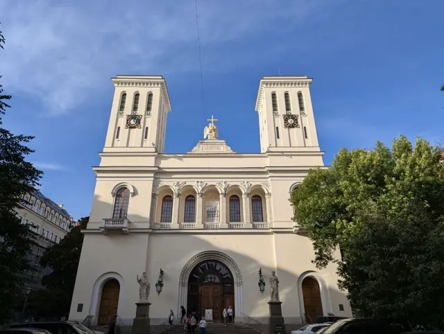 a twin-towered lutheran church in low sun, people sitting on the steps under the arched entrance